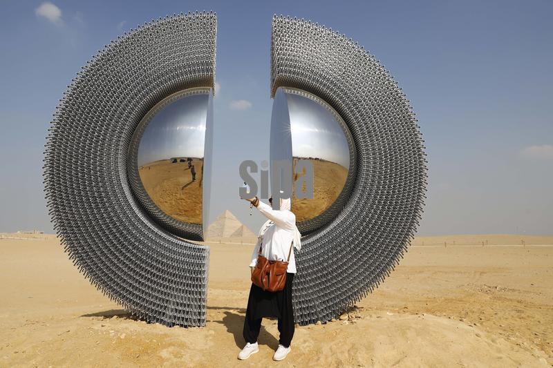 (251112) -- BEIJING, Nov. 12, 2025 (Xinhua) -- A visitor takes a selfie in front of an artwork exhibited during the "Forever Is Now" international art exhibition at Giza Pyramids scenic spot in Giza, Egypt, Nov. 11, 2025.
  The fifth edition of "Forever Is Now" international art exhibition on Tuesday kicked off in the area of Egypt's Giza Pyramids scenic spot, showcasing 10 artworks of artists from different countries. The exhibition runs from Nov. 11 to Dec. 6. (Xinhua/Ahmed Gomaa) (Photo by Xinhua/Sipa USA)